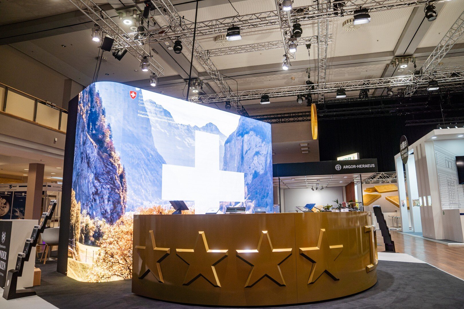 Individueller Messestand von Swissmint mit großer, gebogener LED-Wand und goldener Theke der Eidgenössischen Münzstätte.